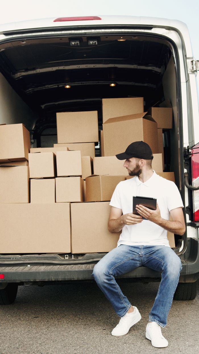 Mastering the First Impression: Your intriguing post title goes here A courier sitting by a van filled with packages, using a digital tablet.