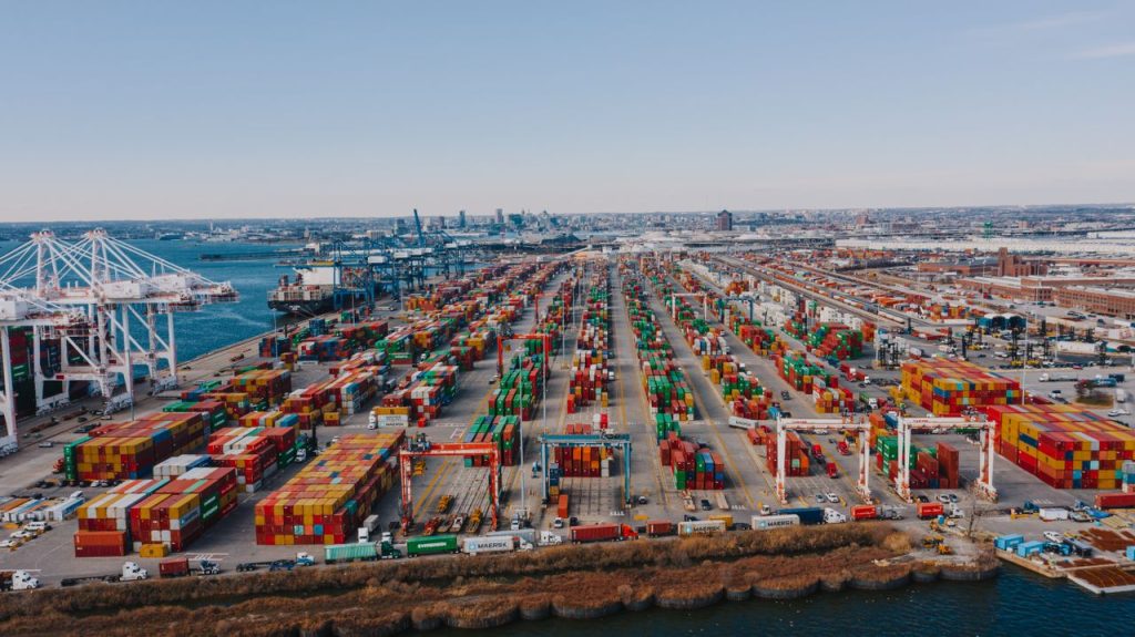 Drone view of river embankment with various bright cargo containers near steel lifting cranes under cloudless sky